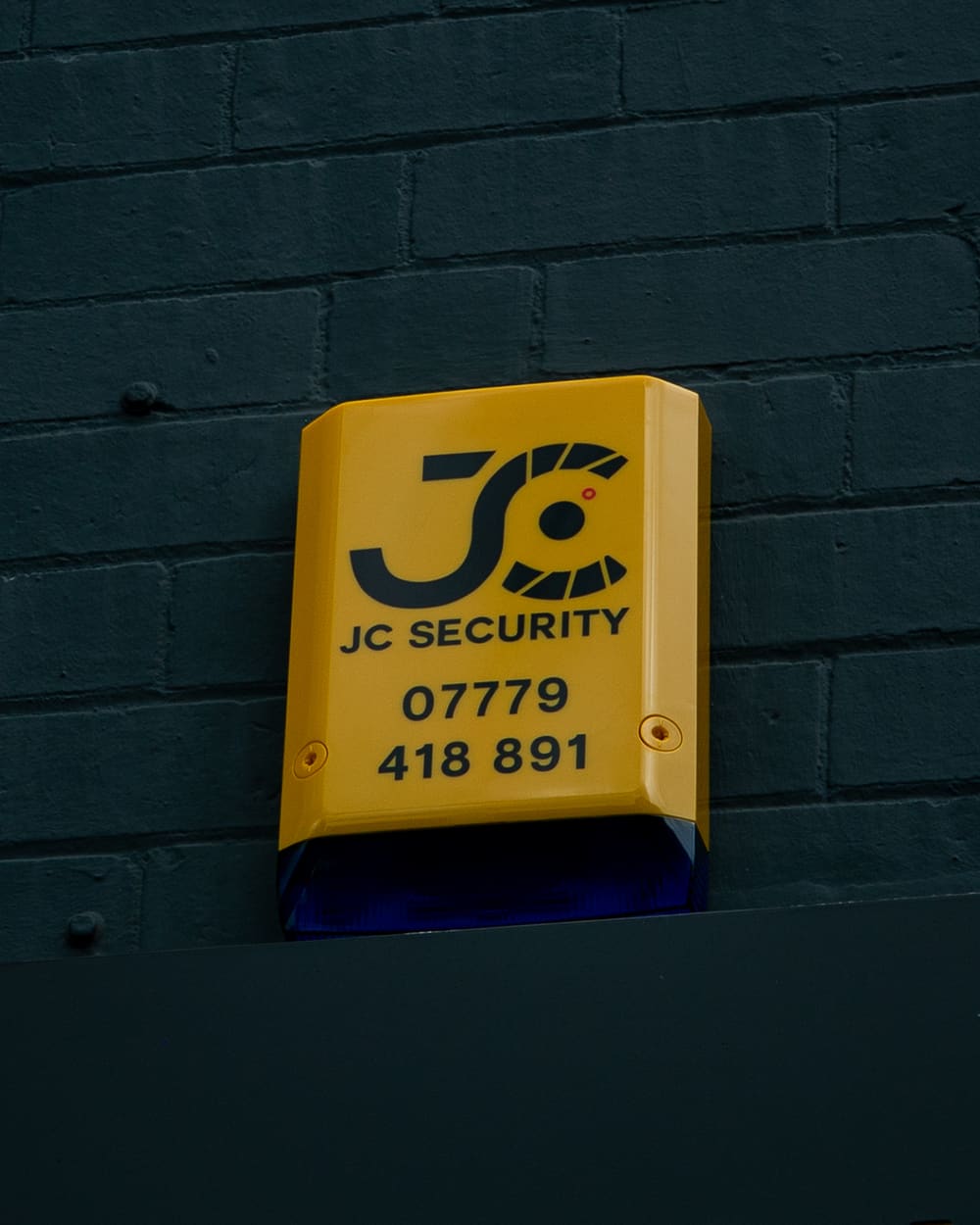 JC Security branded alarm siren installed on an exterior wall